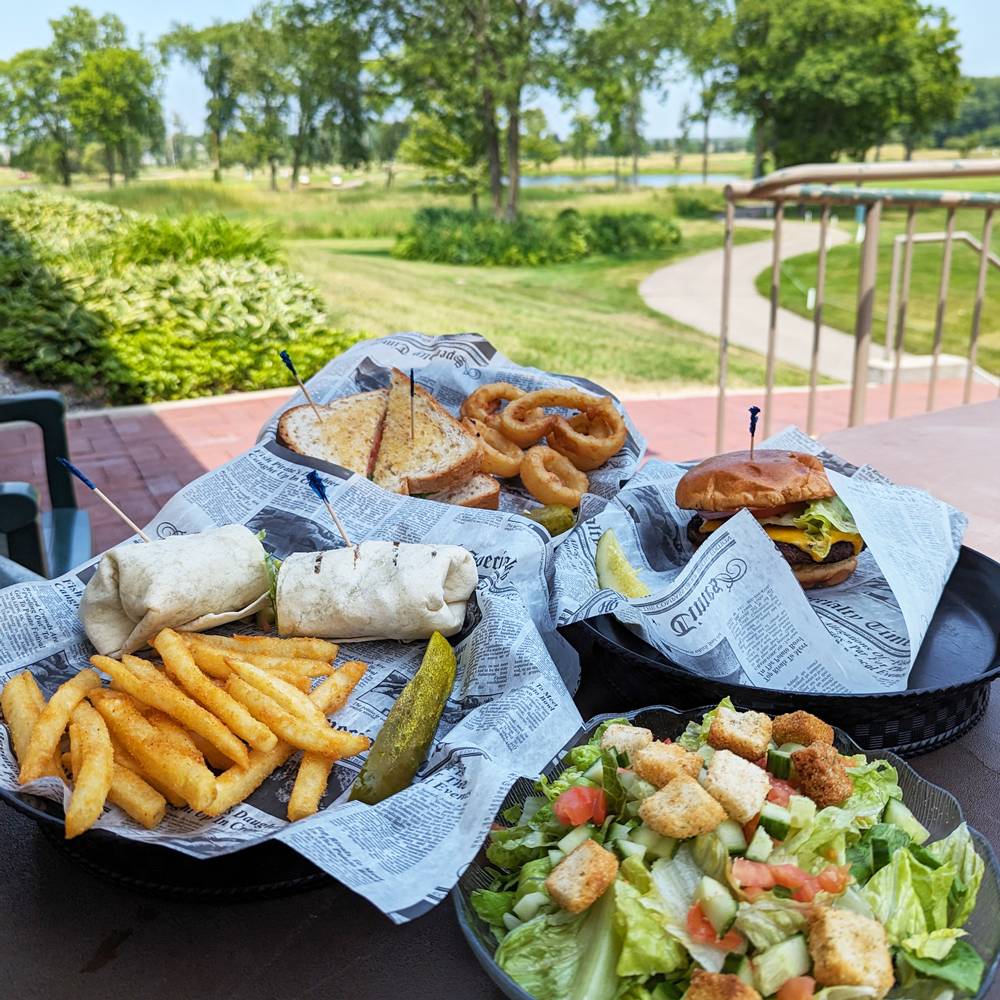 Four plates of food on an outdoor patio table overlooking the Meadows golf course